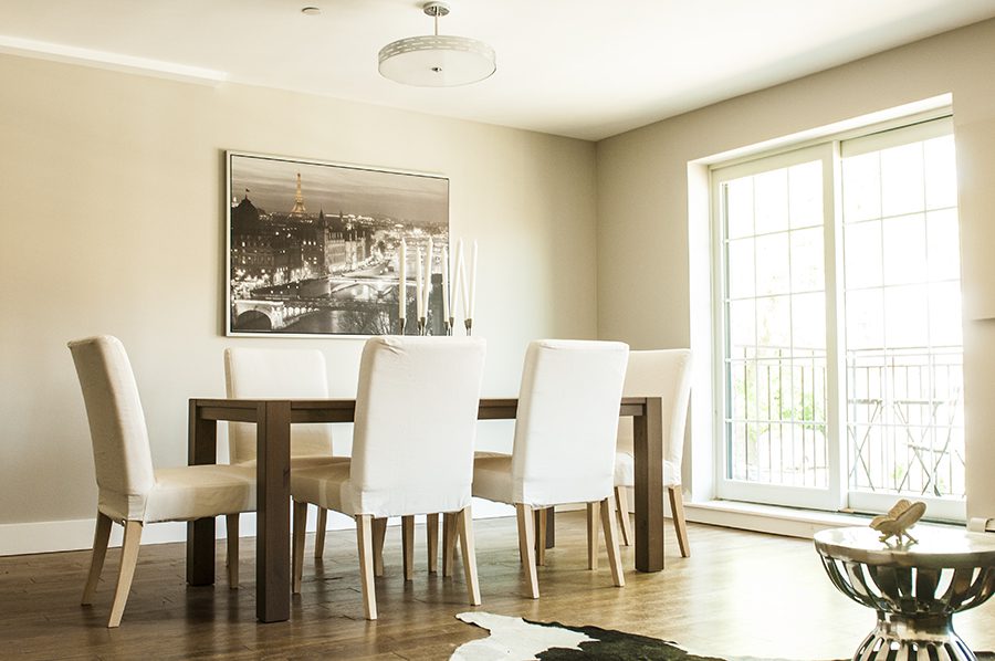 A dining room table with white chairs and a picture on the wall.